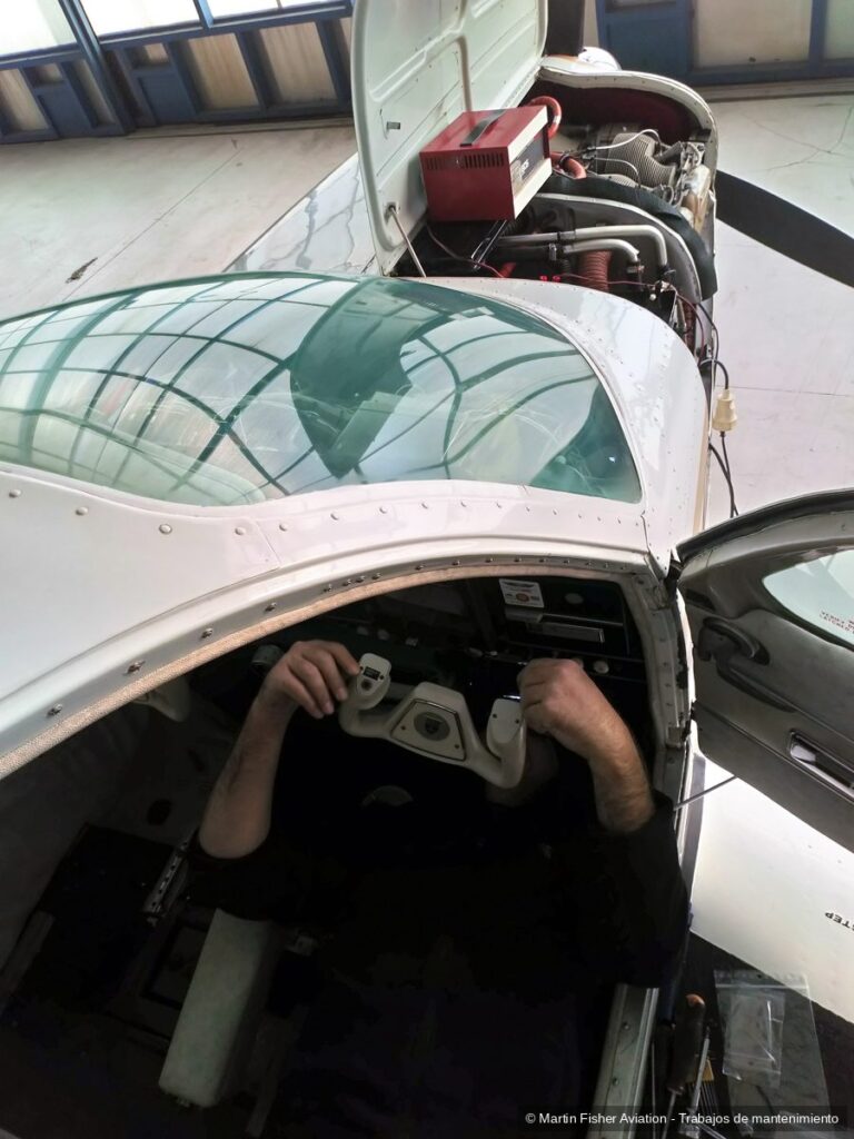 Técnico trabajando en los mandos de un monomotor con el capó del motor abierto